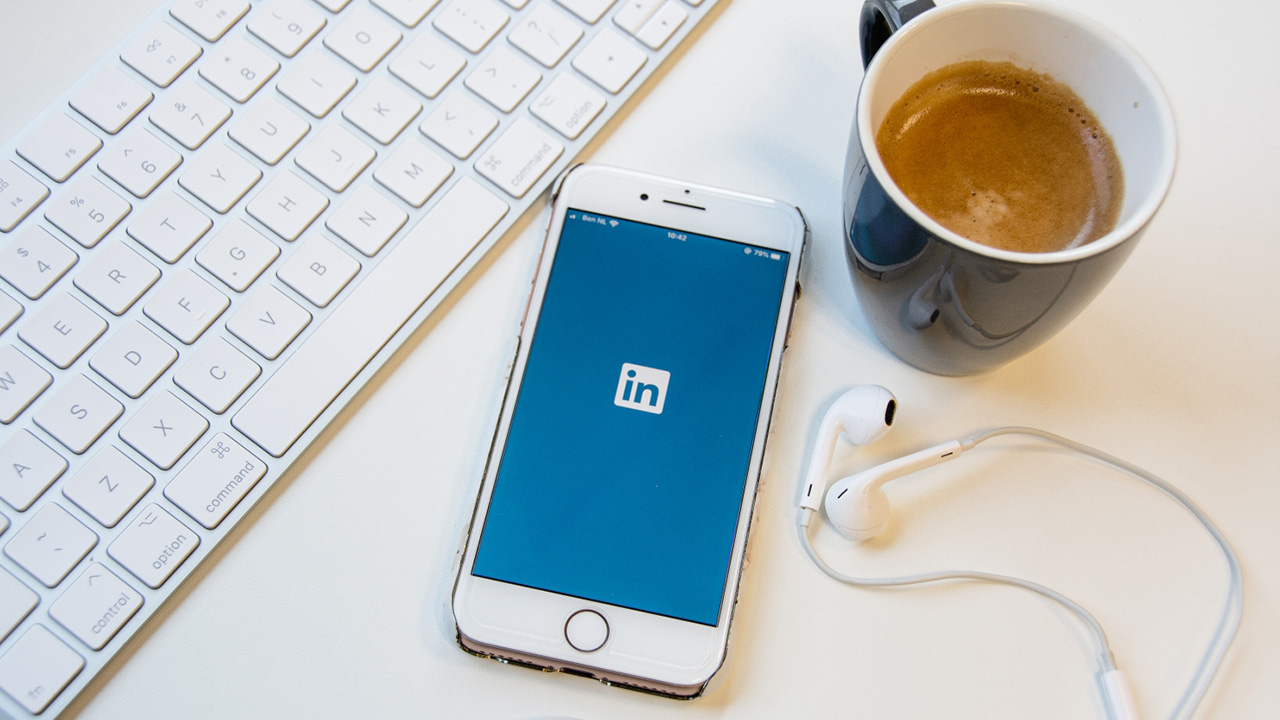 Telefoon naast toetsenbord op bureau met LinkedIn geopend.